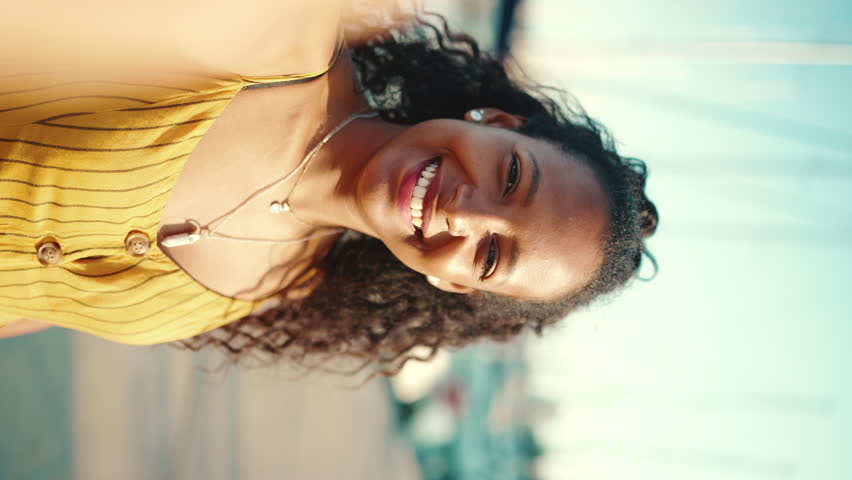 VERTICAL VIDEO, Close-up portrait of smiling girl with long curly hair taking a selfie on the embankment, on yacht background. Frontal closeup of happy young woman looking at camera