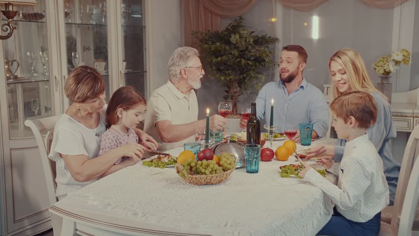 Multigenerational family happily smiling and clinking glasses together in a toast while having holiday dinner party at home