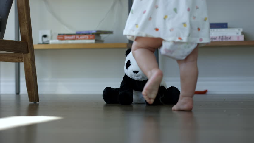 Baby girl walks over and sits down with her stuffed animal toy - wide shot Royalty-Free Stock Footage #1100749783