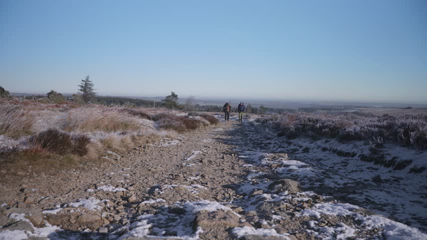 Two men hiking up a beautiful, snowy, frozen trail in a wild, countryside environment. A winter blue sky in the background.