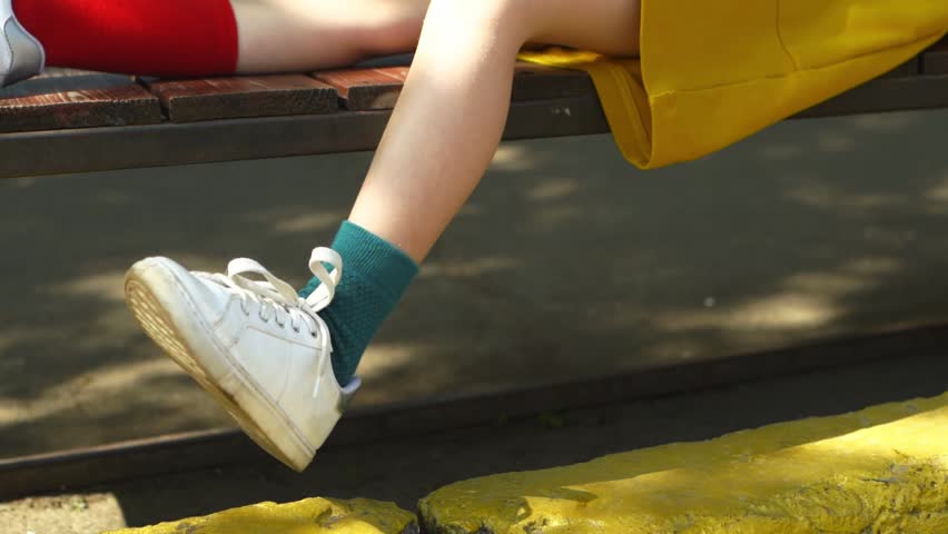 Girl in different socks sits on bench and shakes his leg