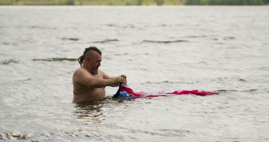 A bearded man pulls the american flag out of the water and looks at the camera. Tourist