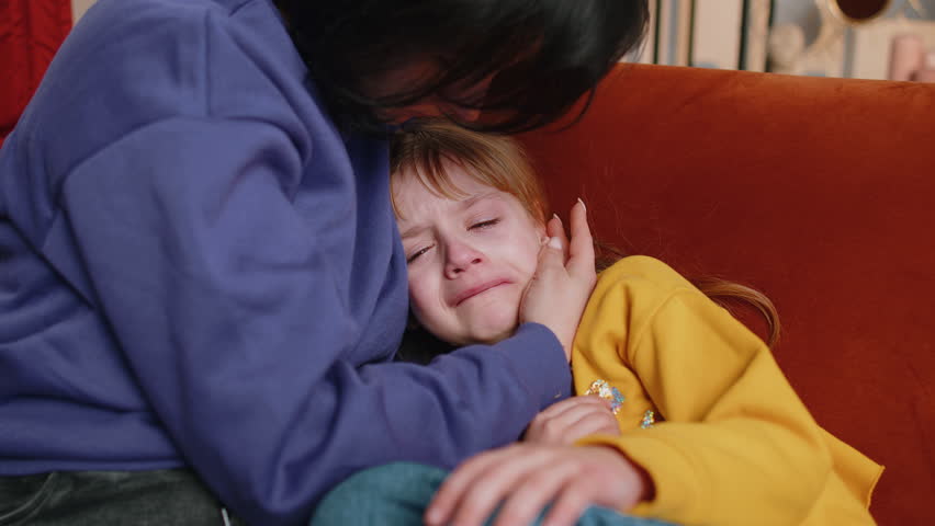 Offended sad girl kid is crying and lying on mother at home. Violence against children in family. Quarrel, bullying at school. Child toddler abuse. Mom hugs, embrace, takes pity on her daughter Royalty-Free Stock Footage #1100756913