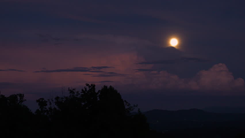 Dramatic evening sky with full moon and storm clouds rolling over countryside. Thunderbolt flashing in huge cumulonimbus cloud. Unsettled atmosphere with moonlight and approaching summer rainstorm.