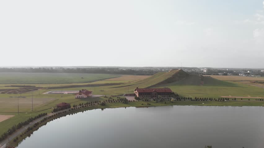Large empty tourist countryside recreational complex with sports grounds, pine park, ski slope and lake without guests. Red roof hotel has satellite dishes. Aerial view in evening on sunny summer day.