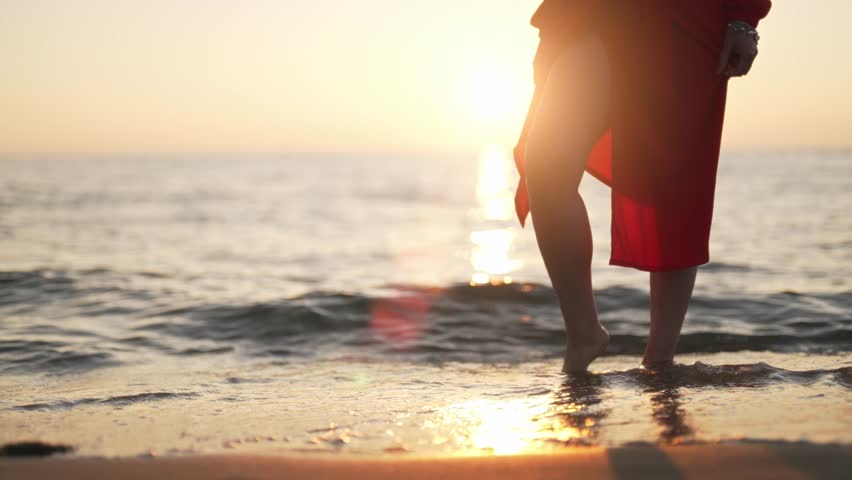 Woman in red stands in the sea at sunset.