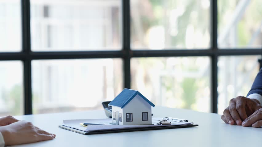 real estate agent helping clients read and sign contract documents at their desks with house designs. along with home insurance