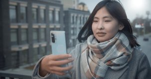 Close-up. A young Asian woman communicates via video link against the backdrop of a bright winter sun, smiles, laughs. Video for social networks, online. Happiness.