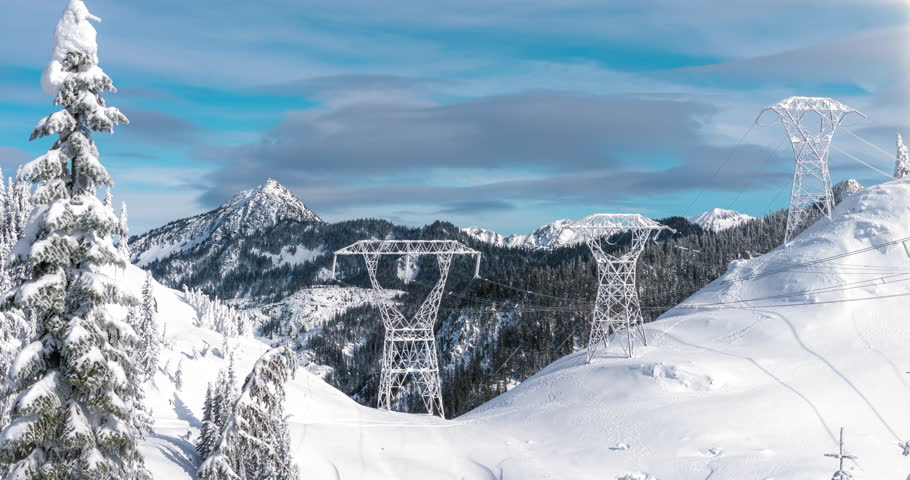 Electrical Powerline Transmission Towers in Mountain Snow Timelapse. Tall Power Grid Structures with Cables Stretching Across Forest Valley in Winter Season with Blue Sky