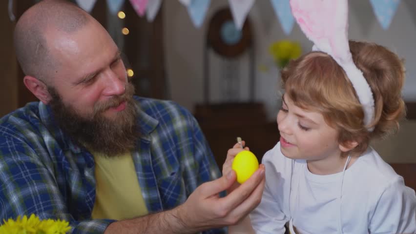 Easter Family traditions. Dad and preschool happy child daughter with bunny ears playing and paint with Easter decorated eggs together at Easter sunday holiday