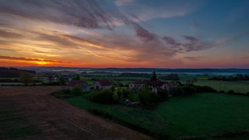 Aerial timelapse of the sun setting over a large farmhouse in the rural countryside