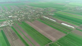Lovely aerial view of a vast agricultural field with different colors and textures. Big greenhouses are in the middle of the field