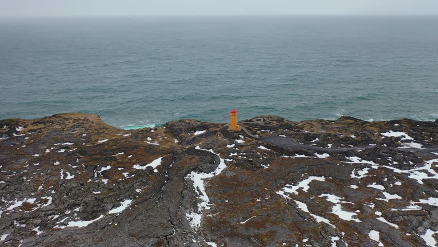 4K aerial footage of an orange lighthouse in northern Iceland on a snowy day in winter.
