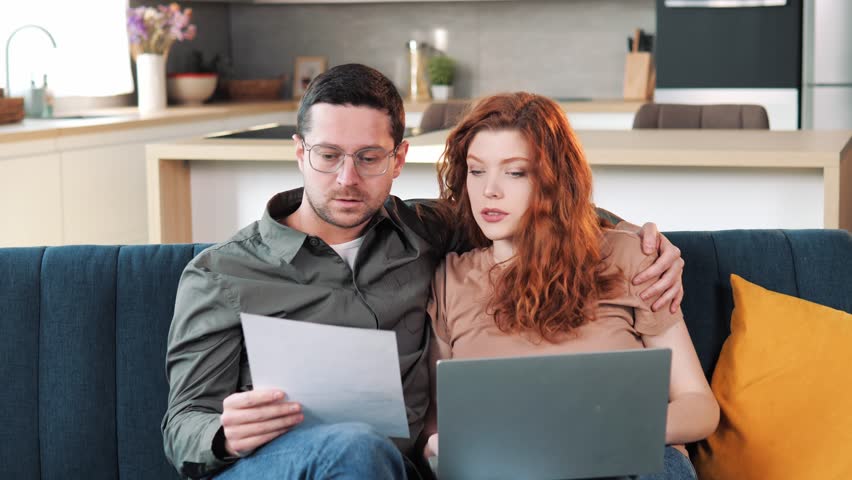 Couple sit on couch with laptop holding document pay bills, payment of the fine count expenses, make budget control, manage finances, review overdue loan payments feel stressed. Crisis, lack of money Royalty-Free Stock Footage #1100774123