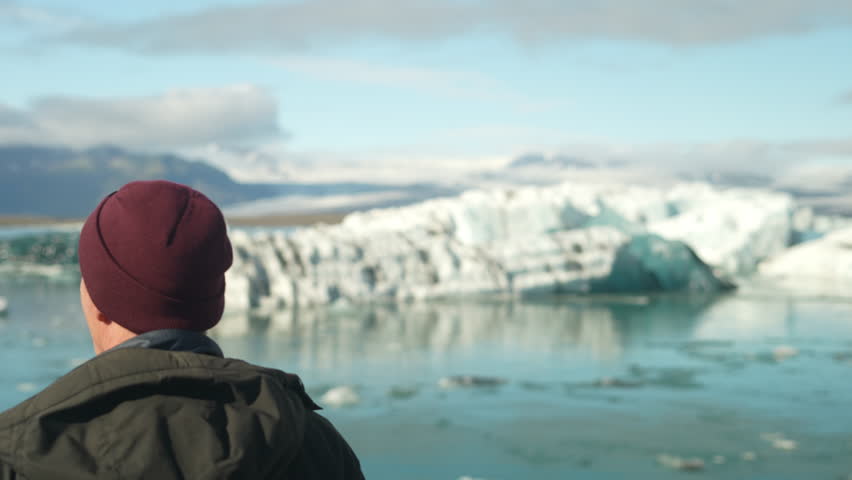 A daytime wide shot, focusing on the back view of a man and Jokulsarlon Glacier Lagoon in Iceland