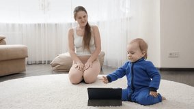 Young mother with little baby son doing sports on carpet and watching training video on tablet computer. Family healthcare, active lifestyle, parenting and child development.