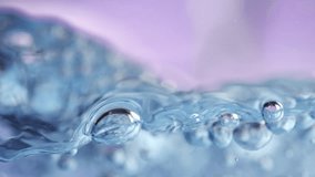 slow motion video of water bubbles in blue light in front of a purple background 
