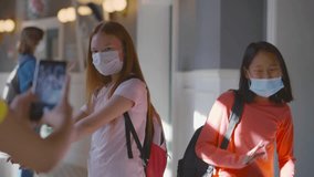 Teenagers in medical mask shooting together dancing video on mobile phone for social media at school. High school girls students make content for internet blog on smartphone. Realtime