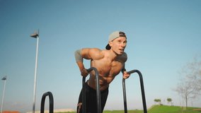 Muscular man doing push ups exercises on parallel bars. Male athlete workout outdoor gym, Strength and motivation. Medium shoot front view. Bodyweight training. Modern calisthenics park - Powered by Shutterstock - Get 15% off with code: PIKWIZARD15