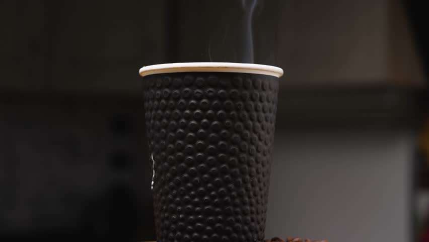 Close-up of a black coffee paper cup. The camera rotates around. Steam rises from the cup. Parallax effect. The concept of a coffee shop. Coffee as a way of life of modern man. Slow motion Royalty-Free Stock Footage #1100781563