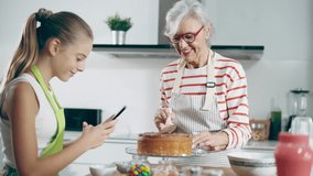 Video of cute granddaughter taking photos with her smartphone while grandmother making tasty chocolate cake in the kitchen. - Powered by Shutterstock - Get 15% off with code: PIKWIZARD15