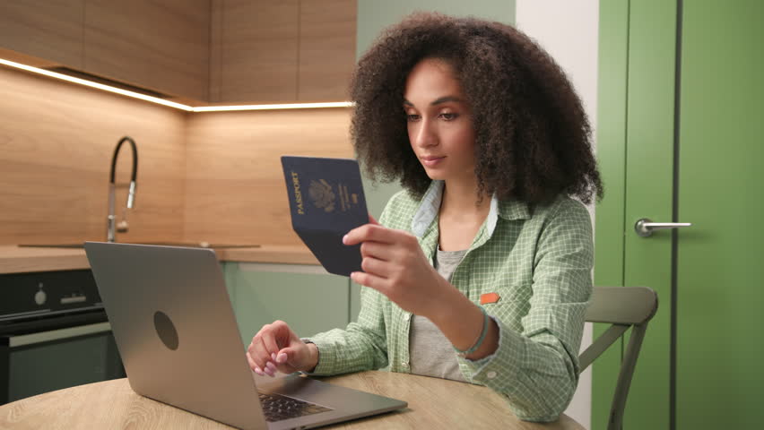 Mixed Race Woman Holding US Passport Using Laptop. Female filling application form holding ID document. Royalty-Free Stock Footage #1100783941