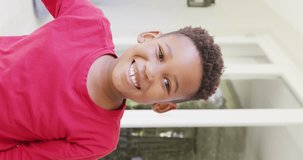 Vertical video of portrait of happy african american boy looking at camera, in slow motion. Spending quality time, domestic life and childhood concept.