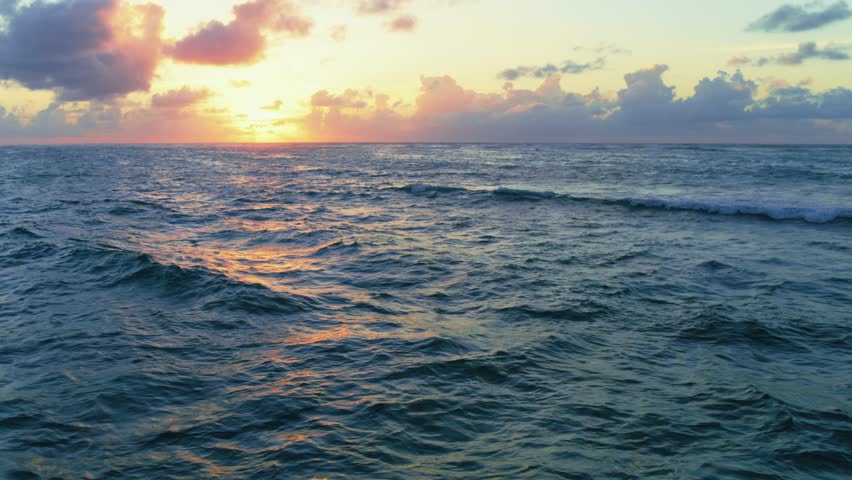 Sunset over the sea on a summer tropical evening. Sea waves with a reflection of the setting sun. Ripples of water with sunbeams. Deep blue ocean under orange skies. Twilight over the sea.