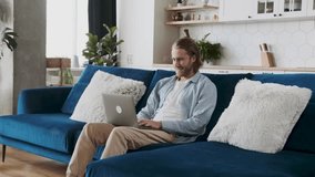 A male employee working remotely in his living room on a laptop, writing report with a pleasant smile. Casually dressed male emploee. - Powered by Shutterstock - Get 15% off with code: PIKWIZARD15