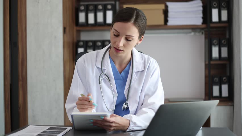 Woman doctor consulting with patient online at desk in hospital, female doctor physician wearing white coat using laptop computer writing notes at workplace, Health care and Medicine concept. | Shutterstock HD Video #1100794777