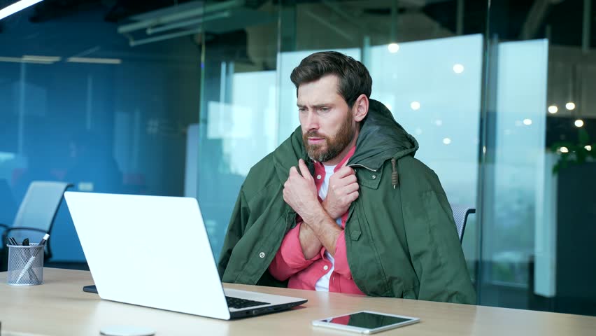 Cold bearded business man freelancer covered by jacket suffers and trembles warms hands try to work on laptop computer at desk in modern office with problem of heating system indoors Low temperature | Shutterstock HD Video #1100795797