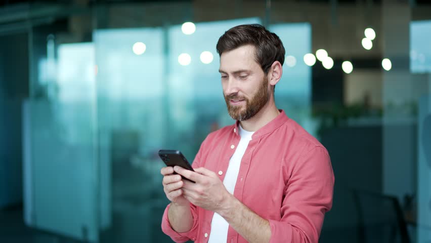 Smiling business man freelancer hold smartphone scrolling and watching social media at modern office workplace Happy bearded entrepreneur employer using phone app typing browsing on break indoor alone | Shutterstock HD Video #1100795829