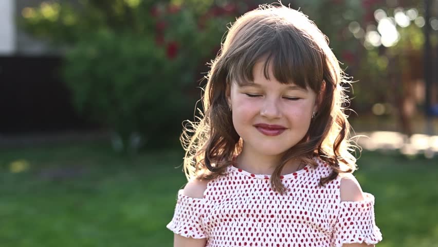 front view of adorable little girl with hairstyle is smiling with her outdoors on summer day. caucasian friendly and shy kid looking at camera posing. Happy childhood on holiday vacation.