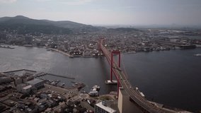 Cinematic drone flyover of red bridge in Japan, kitakyrushu wakato bridge, city in the background and river in the middle
