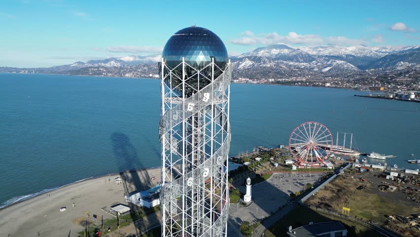 Flight around a modern building in a city on the seashore. View from above of the sea, city, ferris wheel and coastline. Alphabet Tower in Batumi city, Georgia