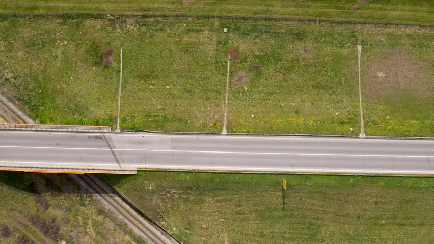 Aerial shot of semi truck and two cars on the road over railroad overpass, top view drone pov footage on sunny spring day