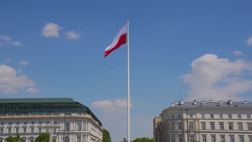 The flag of Poland is blowing in the wind against the background of the sky. 
The flag rises high above the ground.