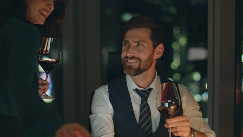 Attractive brunette woman bringing wine to businessman focused on work late night close up. Young happy partners smiling toasting for company success. Two coworkers relaxing together after long day. Royalty-Free Stock Footage #1100805677