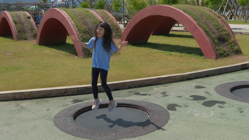 Girl feel the freedom on trampoline. A happy smiling child fee the freedom and jumping on trampoline on playground under sun.