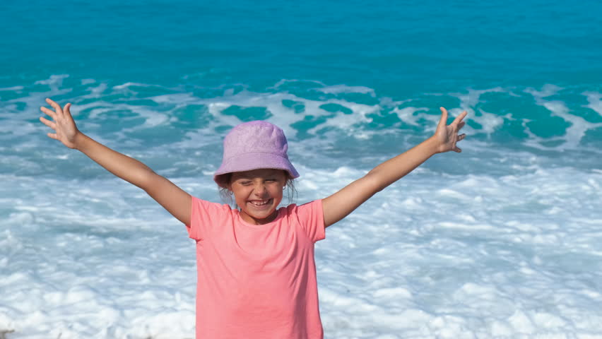 Creative child on pebbles shore. A joyful little girl greeting her summer vacation on the beach during vacation time.