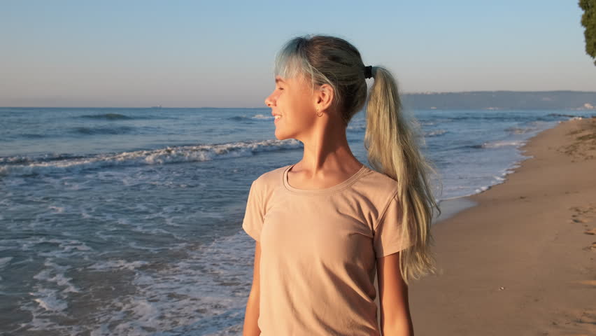 Teen waving hands on seashore. A smiling happy young girl waving her hands on the sandy golden beach during summer holiday.