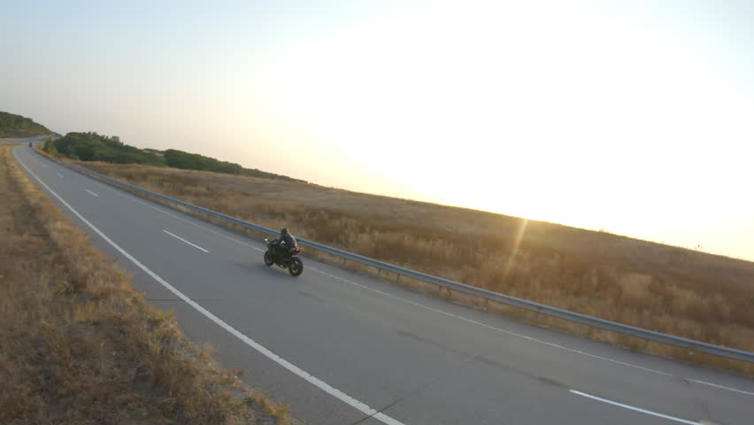 Aerial shot of biker is riding on modern sport motorbike at autumn highway. Motorcyclist racing his motorcycle on country road at sunset. Man drive bike during trip. Concept of freedom and adventure | Shutterstock HD Video #1100806569