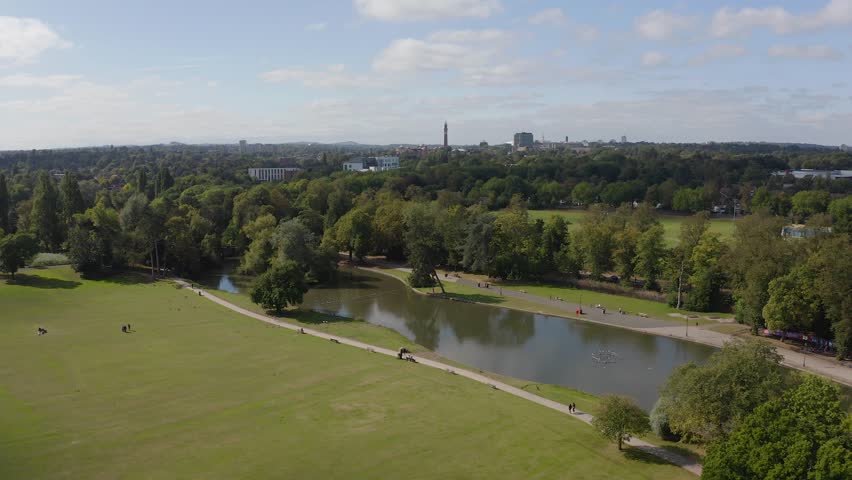 Cannon Hill Park, Birmingham on a glorious summer day. 4k Drone shot looking over the lake, towards Old Joe Clock Tower at the University of Birmingham.