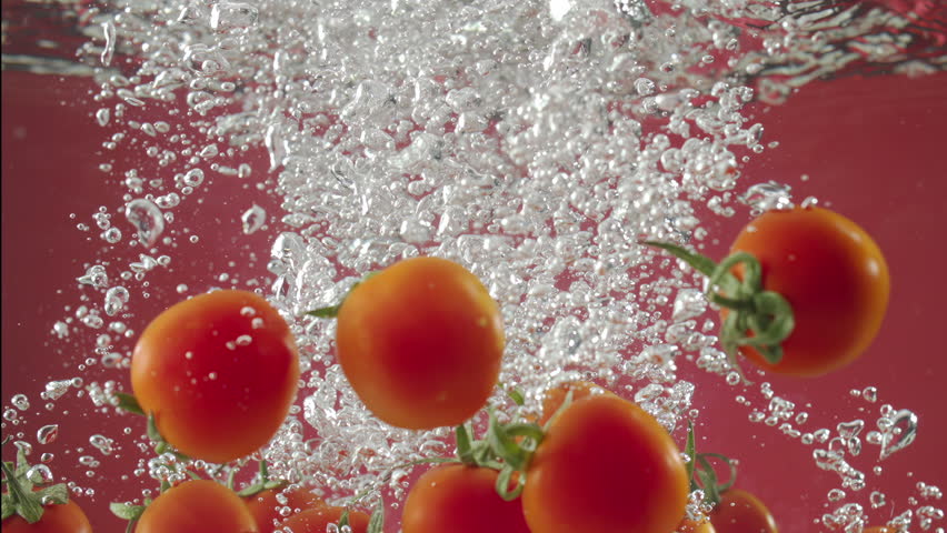 Slow motion of red cherry tomatos falling into water on red background