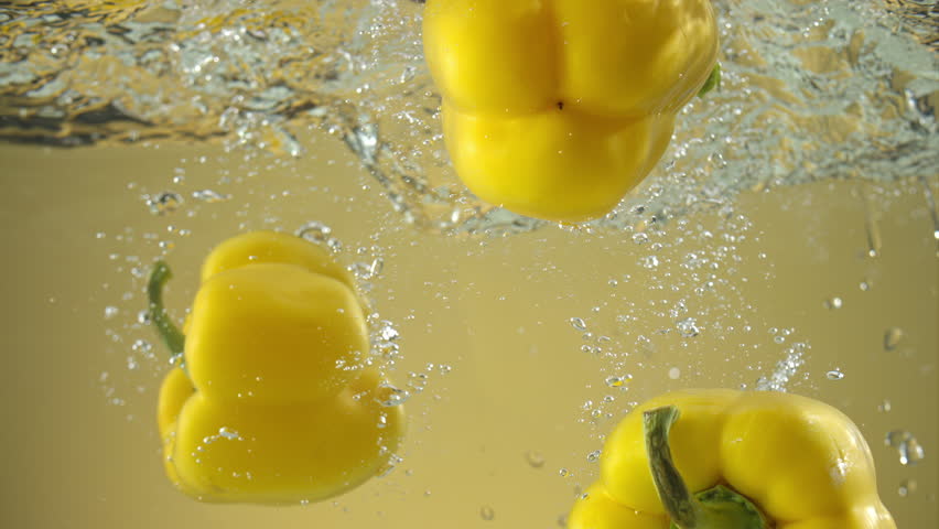 Slow motion of yellow peppers falling into water on yellow background