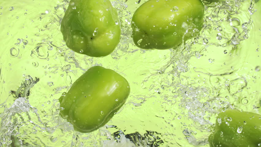 Slow motion of green peppers falling into water surface on green background