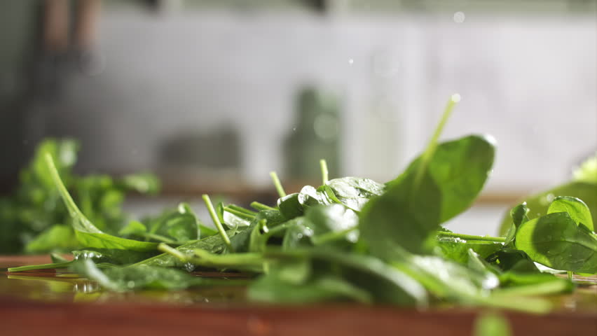 Slow motion of fresh baby spinach falling on wet wooden board in a kitchen