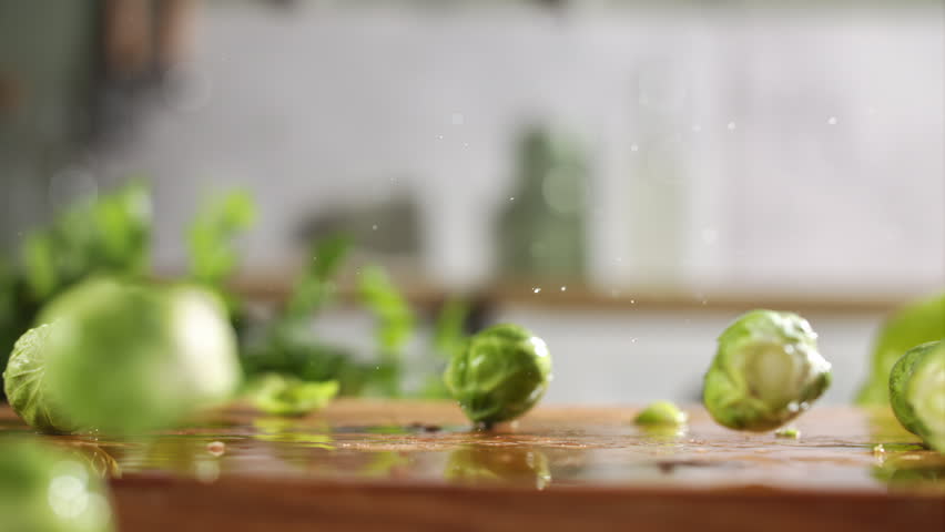 Slow motion of fresh brussels sprouts falling on wet wooden board in a kitchen