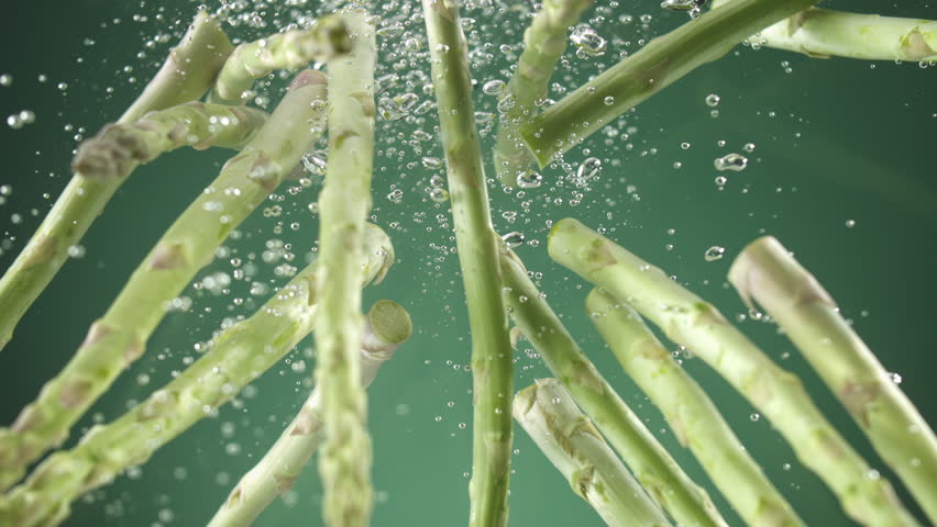 Slow motion of Fresh raw asparagus falling into water on green background