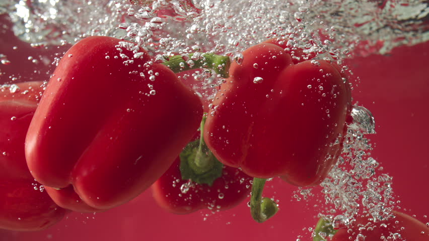 Slow motion of red peppers falling into water on red background
